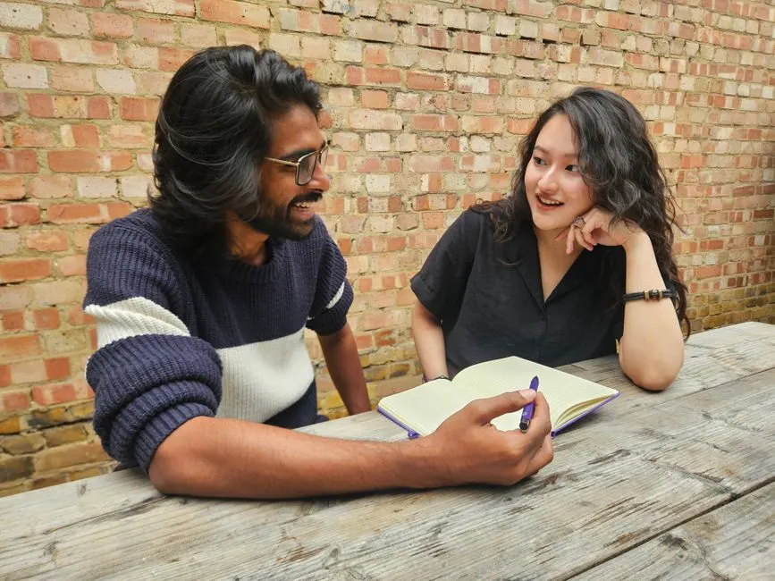 Dos personas hablando ante un cuaderno abierto en una mesa de madera