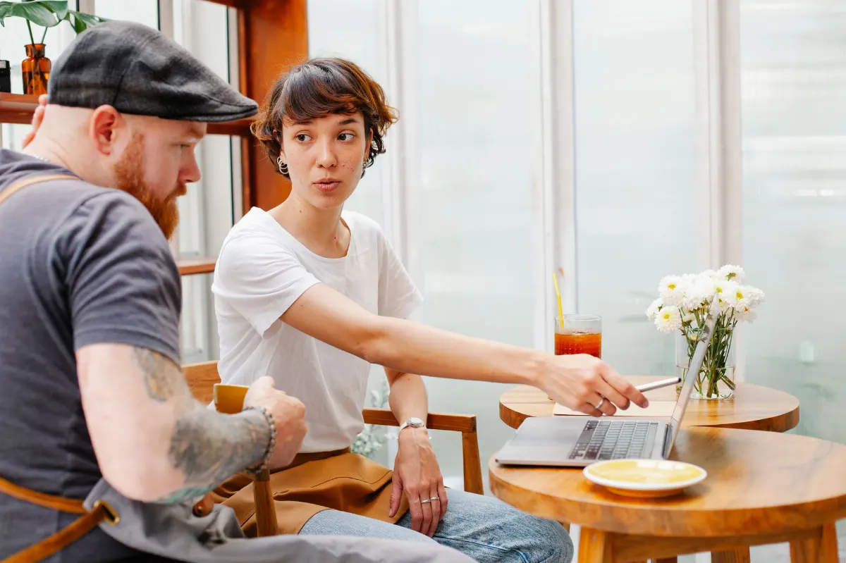 Dos personas conversando en la mesa de una cafetería junto a la ventana