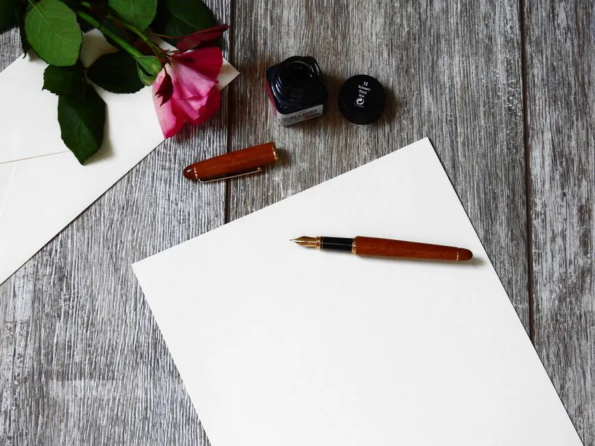 Una hoja en blanco con una pluma, un sobre y una rosa sobre madera
